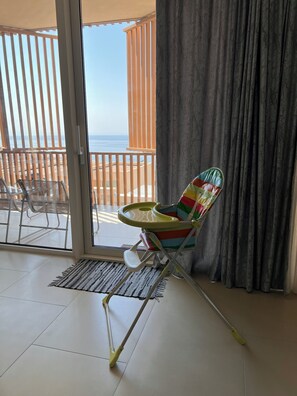 Una habitación con vista a la playa, una silla colorida, un trapeador y un ventanal corredero.