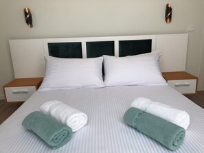 Una habitación de hotel con una cama grande, dos almohadillas blancas, dos mesitas de noche y dos toallas enrolladas.