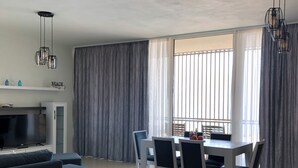 A modern living room with a sofa, TV, dining table, chairs, and a kitchen area. - Cosy apartment in Green Coast Albania-blue flag beach (Palasë)