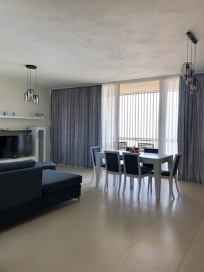 Ein modernes Wohnzimmer mit einer Couch, Fernseher, Esstisch, Stühlen und einer Küchenzeile.
