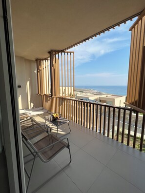 Un balcón con mesa y sillas, vista al mar y barandilla de madera.