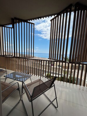 Ein Balkon mit Glastisch und -stühlen, Holzgeländern und Blick auf Strand und Meer.
