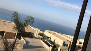 A coastal view from a balcony with a clear sky, a palm tree, and a beach in the background. - Cosy apartment in Green Coast Albania-blue flag beach (Palasë)