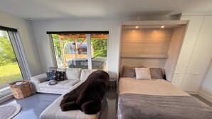 Quarto moderno com cama grande, sofá e janela com vista para uma floresta.
