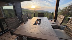 Um deck de madeira com mesa, cadeiras, lareira e vista para a paisagem.