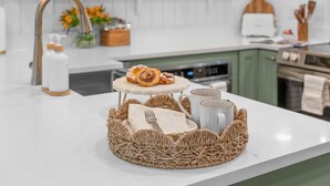 Une cuisine avec un plan de travail blanc, un set de table en fibres tressées, un croissant, deux tasses et un grille-pain.