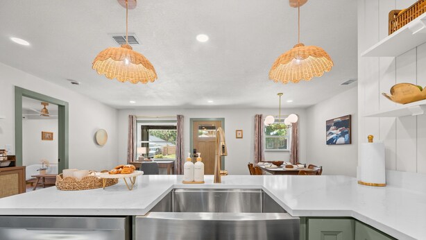 Une cuisine moderne dotée d’un évier en acier inoxydable, de deux luminaires suspendus et d’un coin repas avec une table et des chaises.