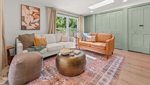 Un salon avec un canapé blanc, un canapé orange, un pouf à motifs et une table basse ronde.