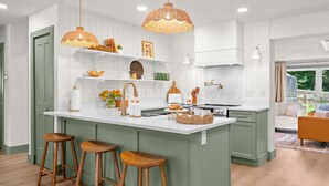 Une cuisine moderne dotée d’un îlot central, de tabourets en bois, de luminaires suspendus et offrant une vue sur l’espace de vie.
