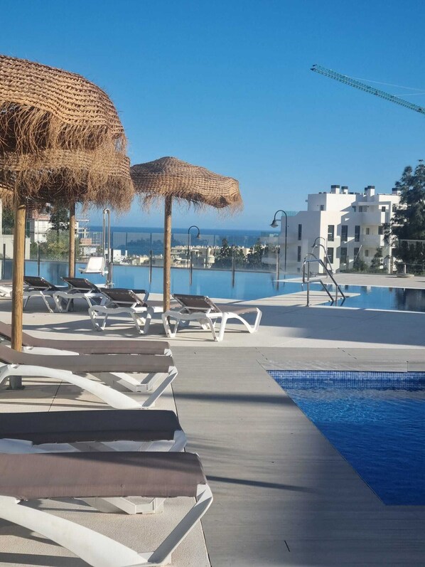 A rooftop pool area with lounge chairs, a small pool, and a view of the sea.