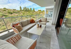 A balcony with a sofa, a table, and a chair, overlooking a hilly landscape.