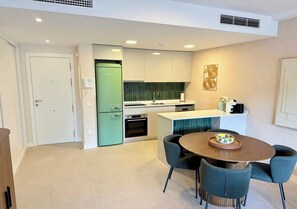 Eine moderne Küche mit einem grünen Kühlschrank, einem Essbereich mit einem runden Tisch und Stühlen sowie einer kleinen Kochinsel mit Spüle.