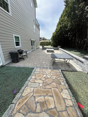 A patio area with stone flooring, a grill, and a seating arrangement.