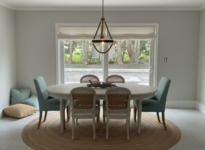 A dining area with a round table, four chairs, a woven rug, and a hanging light fixture.