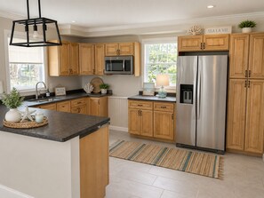 A kitchen with wooden cabinets, stainless steel appliances, a black countertop, and a window with a view.