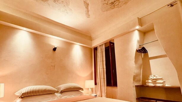Quarto de hotel com uma cama grande, uma mesa de cabeceira, um abajur e um espelho.