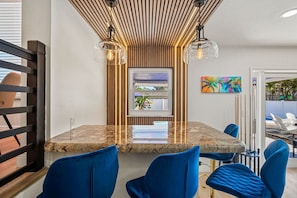 A dining area with a marble table, blue chairs, a wooden slatted ceiling, and a window with a view. - Neon Tropics - Indoor Mini Golf, Pickleball, Pool (Seminole)