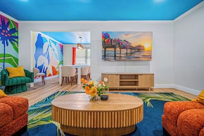 A modern living room with a round wooden coffee table, vibrant artwork, and a colorful abstract mural on the wall. - Neon Tropics - Indoor Mini Golf, Pickleball, Pool (Seminole)