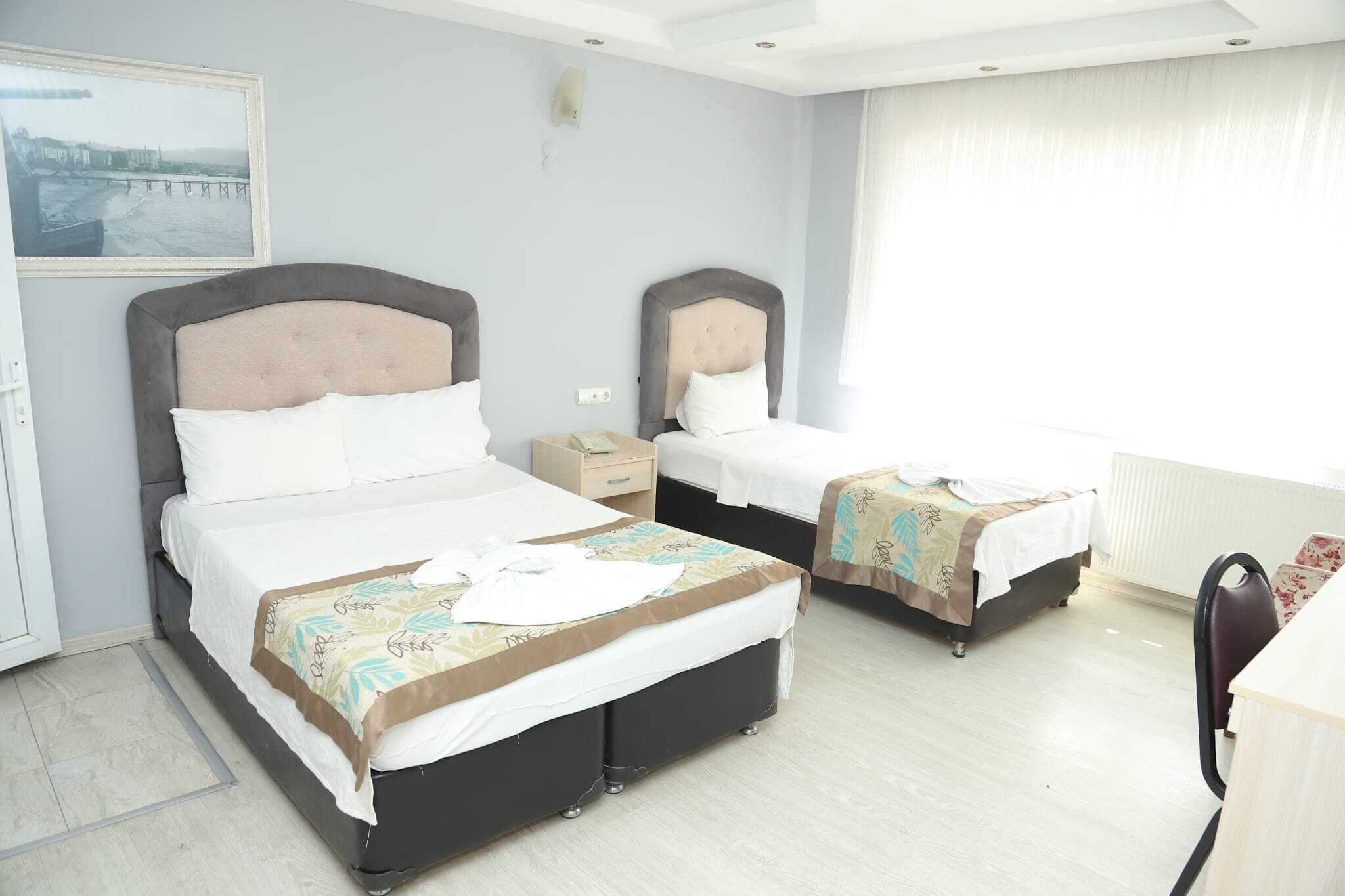 Habitación de hotel con dos camas, un escritorio, una silla, un ventanal con cortinas y un cuadro en la pared.