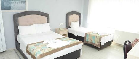 Habitación de hotel con dos camas, un escritorio, una silla, un ventanal con cortinas y un cuadro en la pared.