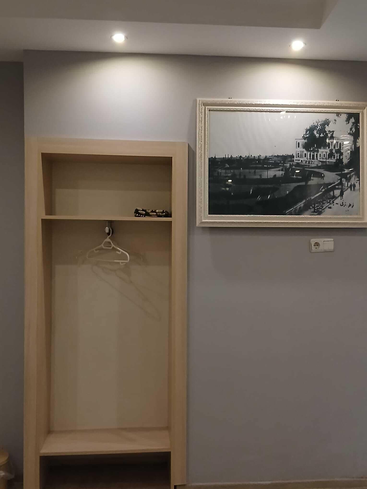Una habitación con un armario de madera, una fotografía blanco y negro enmarcada en la pared y una lámpara en el techo.