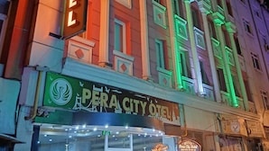 Un edificio con un letrero que dice 'Pera City Hotel' y un cartel verde con un logo de pájaro.