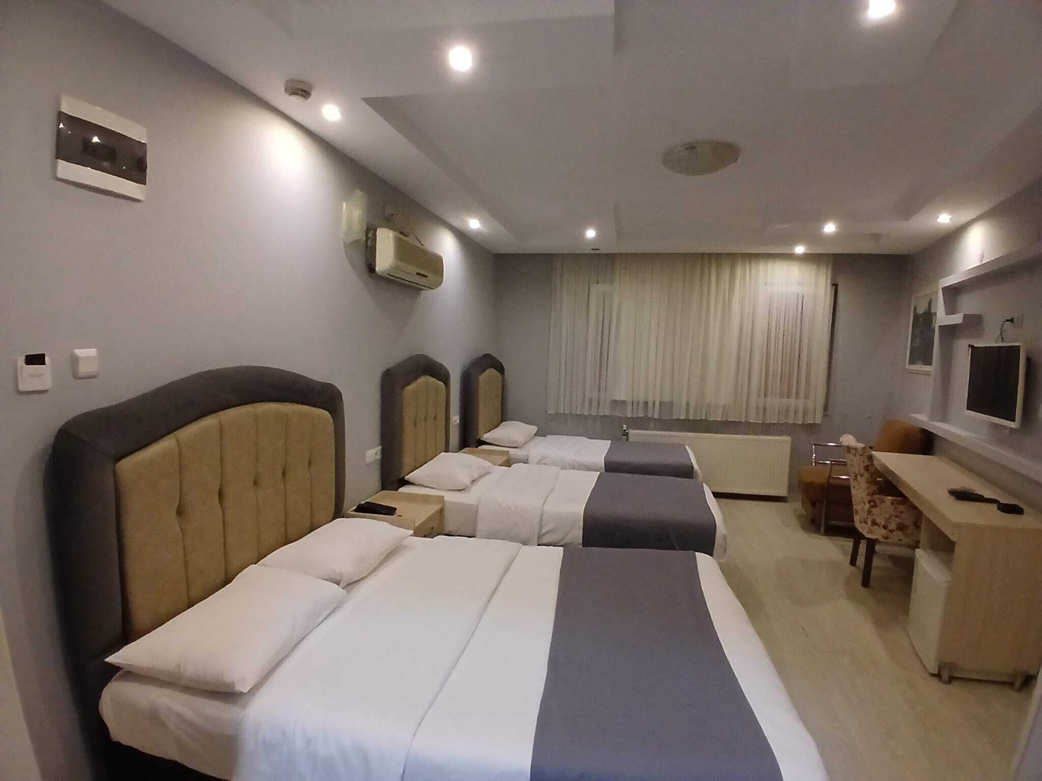 A hotel room with two beds, a desk, a chair, a TV, and a window with curtains.