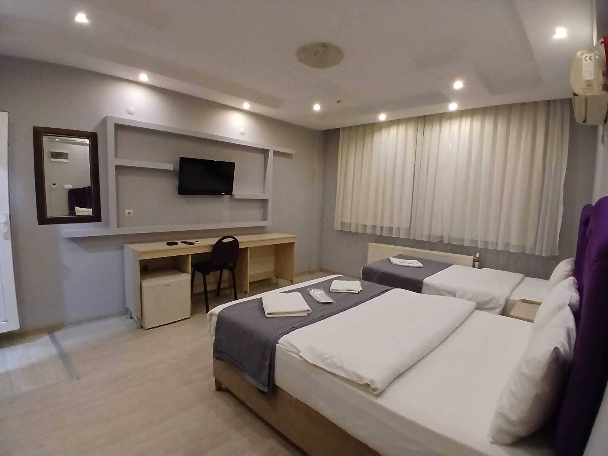 A hotel room with two beds, a desk, a chair, a television, and a window with curtains.