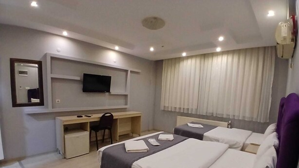 Una habitación de hotel con escritorio, dos camas, televisor y ventana con cortinas.