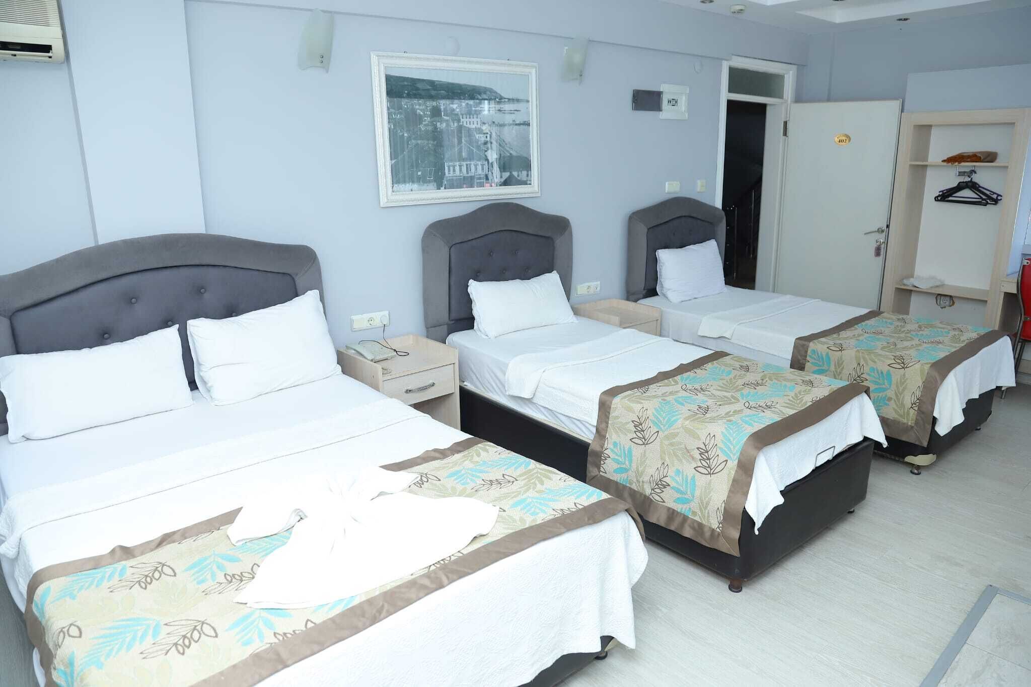 Habitación de hotel con cuatro camas individuales, un armario, perchero y una fotografía enmarcada de un paisaje urbano.