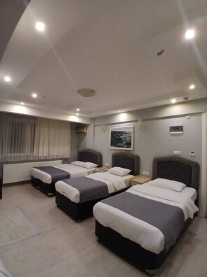Une chambre d’hôtel avec trois lits, une fenêtre avec des rideaux, un tableau encadré au mur et un appareil de climatisation.