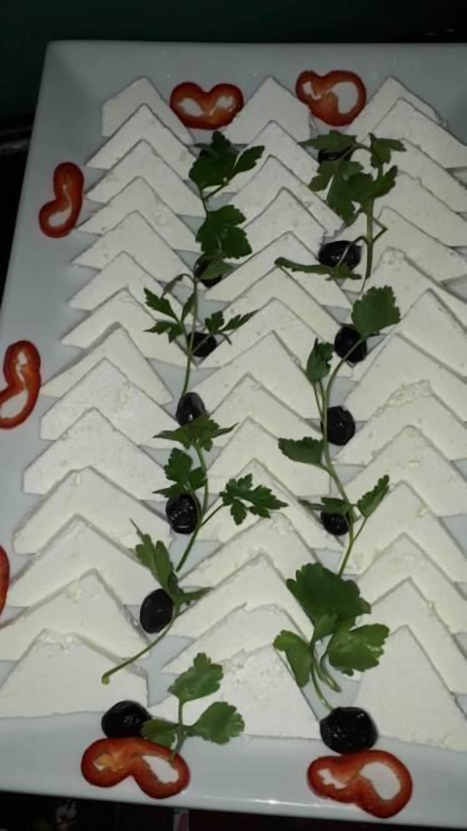 A white plate with a zigzag pattern of food items, garnished with green leaves and black olives.