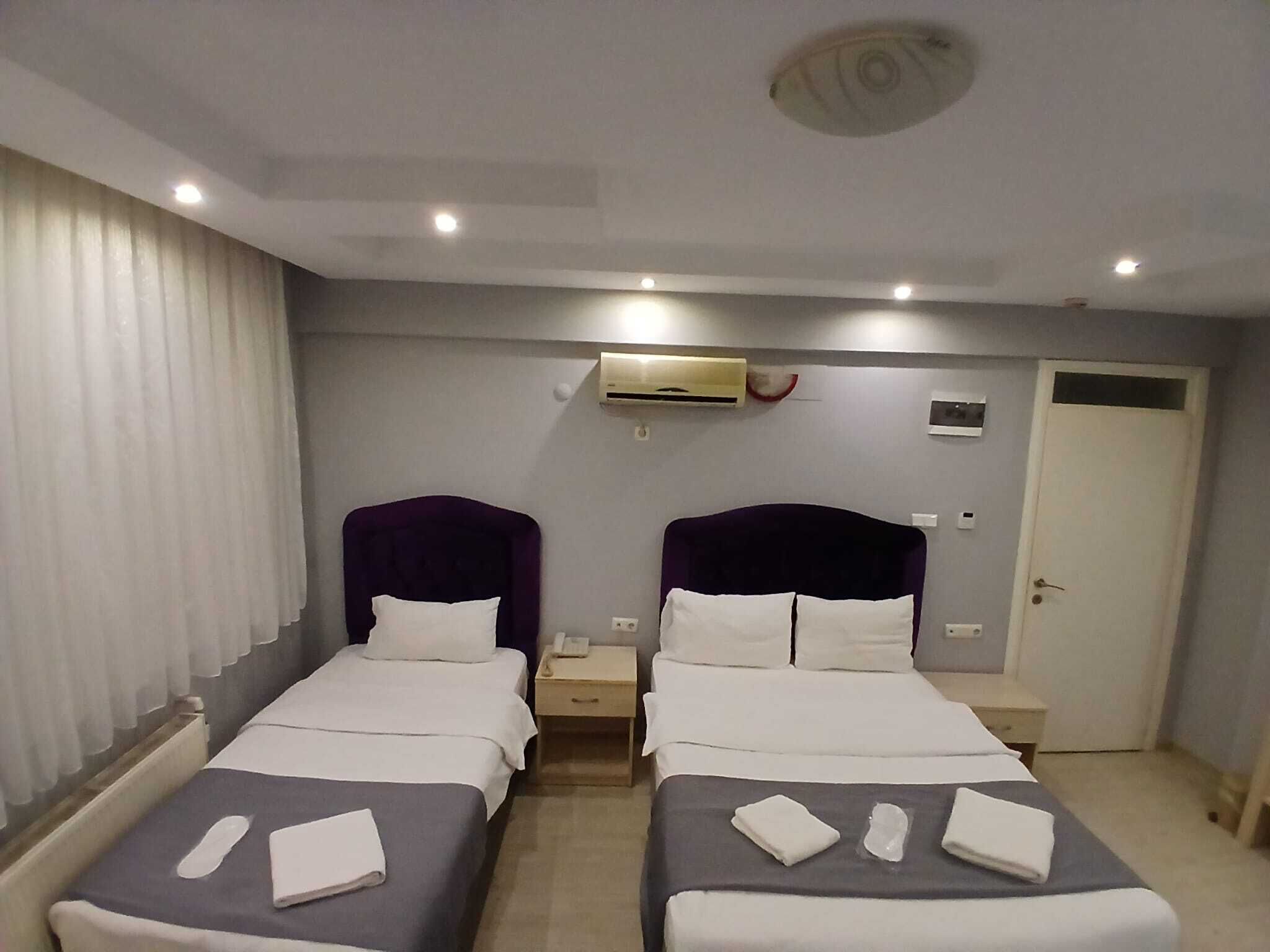 Habitación de hotel con dos camas, una puerta blanca, un equipo de aire acondicionado y una mesita de noche pequeña con un teléfono.