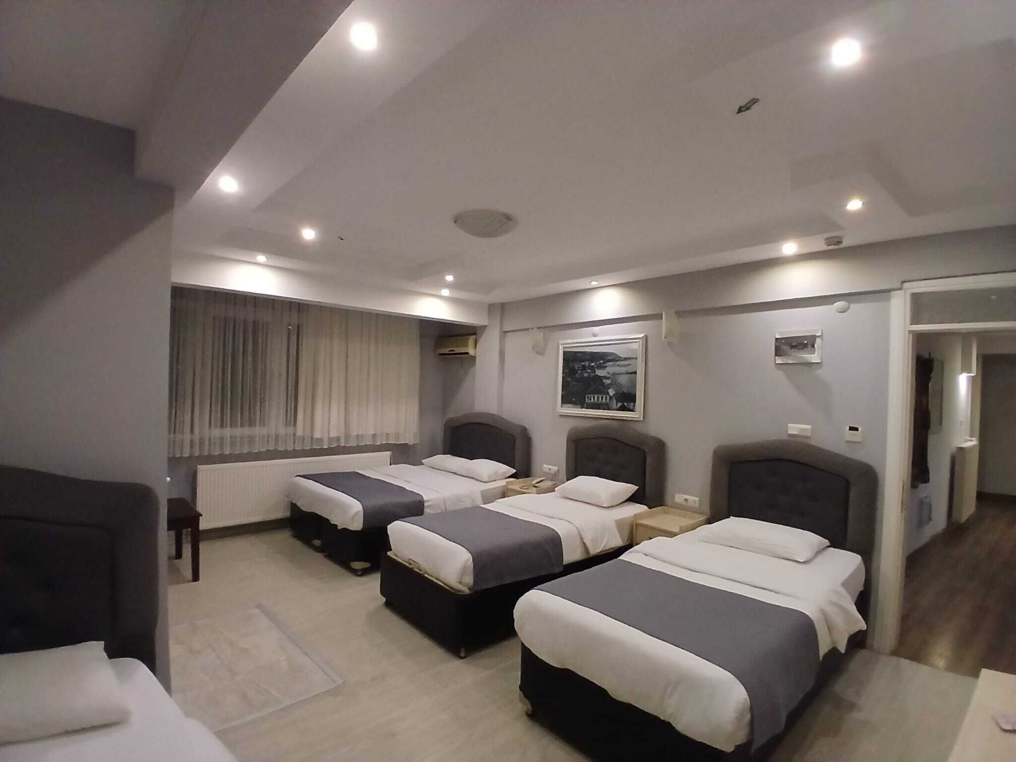 Une chambre d’hôtel avec deux lits, une fenêtre avec des rideaux, un tableau encadré au mur et une porte donnant sur une autre pièce.