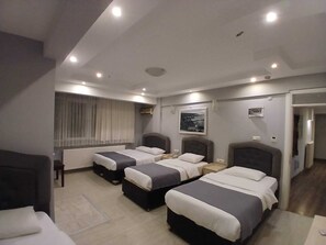 Une chambre d’hôtel avec deux lits, une fenêtre avec des rideaux, un tableau encadré au mur et une porte donnant sur une autre pièce.