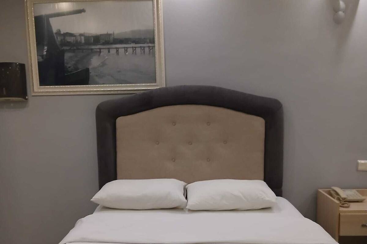 Una cama bien hecha con cabecera, una mesita de noche con un teléfono y un cuadro en la pared.