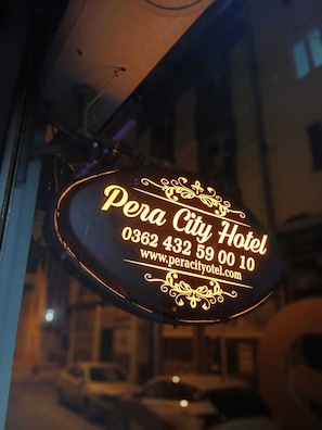Une enseigne lumineuse au néon pour l’hôtel Pera City, avec les coordonnées et l’adresse du site web.
