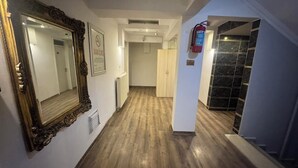 Un pasillo con piso de madera, un espejo grande y ornamentado, y un extintor en la pared.