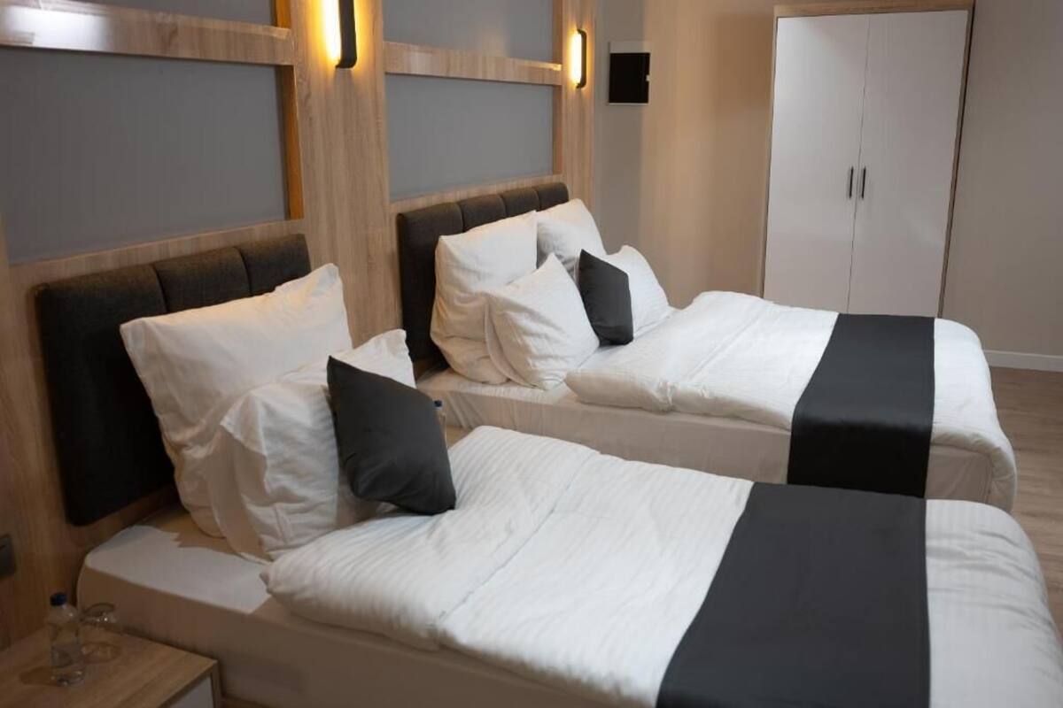 Une chambre d’hôtel avec deux lits, une armoire et une table de chevet sur laquelle se trouvent une bouteille et des verres.