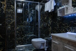 A bathroom with a glass-enclosed shower, a toilet, and a vanity with a sink. - Golden River Hotel by Continent (Arnavutkoy)