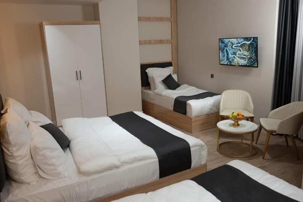A hotel room with two beds, a wardrobe, a small round table with a fruit bowl, and a painting on the wall.