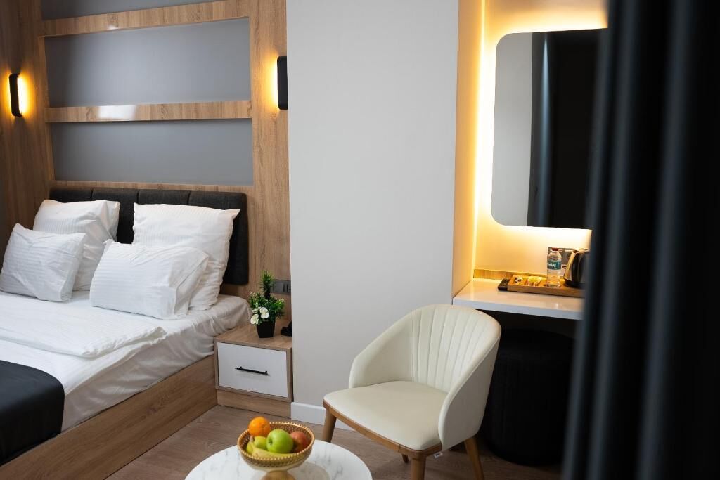 A modern hotel room with a bed, bedside table, chair, and a small table with fruit.