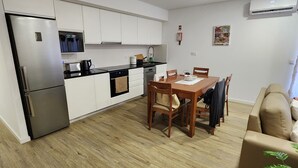 A modern kitchen with white cabinets, a stainless steel refrigerator, and a dining area with a wooden table and chairs.