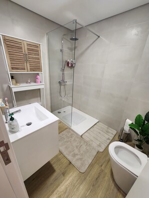 Une salle de bain moderne avec une douche à parois de verre, un lavabo blanc, des toilettes et un meuble en bois.