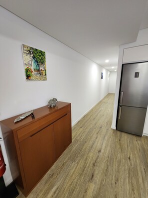 A hallway with a wooden floor, a brown cabinet, a refrigerator, and a wall-mounted painting. - Spacious 3-bedroom apartment with AC in welcoming Sao Miguel (Rabo de Peixe, Sao Miguel)