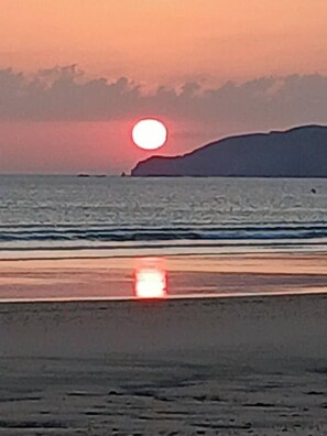 Un tramonto su una spiaggia con acque calme e una terraferma in lontananza.