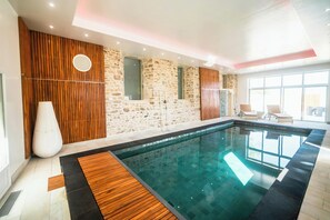 Una piscina con elementi in legno, pareti in pietra e un'ampia finestra.