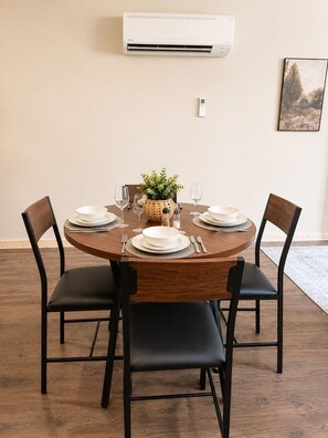 Una mesa de comedor con cuatro sillas, una planta en maceta y un aire acondicionado de pared.