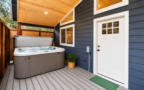 Un jacuzzi en una terraza de madera con una casa al fondo.