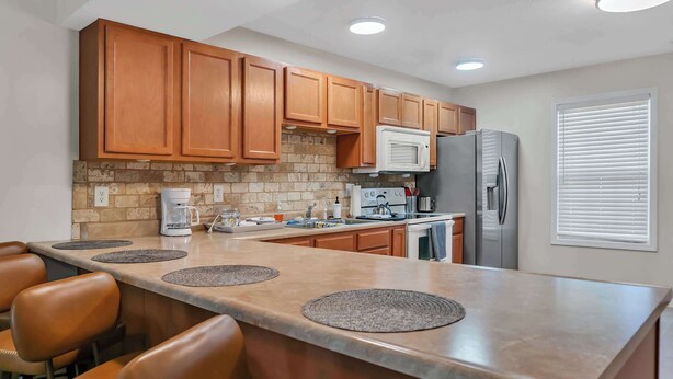 A kitchen with wooden cabinets, a stainless steel refrigerator, a microwave, and a coffee maker. - Cozy Bloomington Townhouse Close to IU Campus (Bloomington)